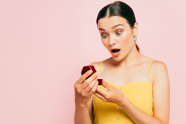 shocked brunette young woman holding box with engagement ring isolated on pink - Fotoğraf, Görsel