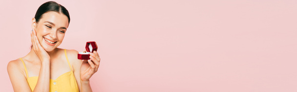 brunetka młoda kobieta gospodarstwa pudełko z pierścionek zaręczynowy odizolowany na różowy, panoramiczny strzał - Zdjęcie, obraz