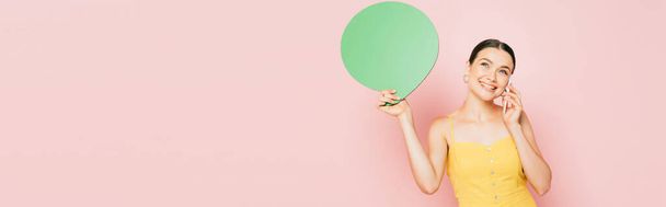 morena mujer joven con verde burbuja habla en blanco hablando en el teléfono inteligente en rosa, tiro panorámico - Foto, Imagen