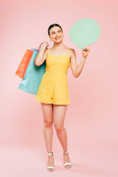 full length view of brunette young woman with shopping bags and speech bubble on pink - Foto, imagen