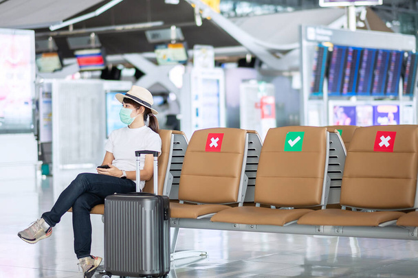 Junge Frau mit Gesichtsmaske und auf einem Stuhl im Flughafen sitzend, Schutz Coronavirus-Infektion (Covid-19), Asienreisende. Neue Normalität, Reiseblase und soziale Distanzierung - Foto, Bild