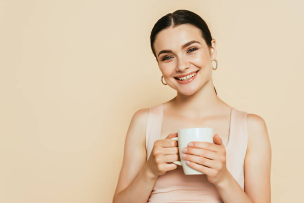brunette young woman holding mug isolated on beige - 写真・画像