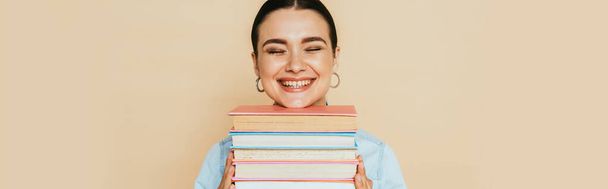 estudiante en camisa de mezclilla con libros sonriendo aislado en beige, plano panorámico - Foto, imagen