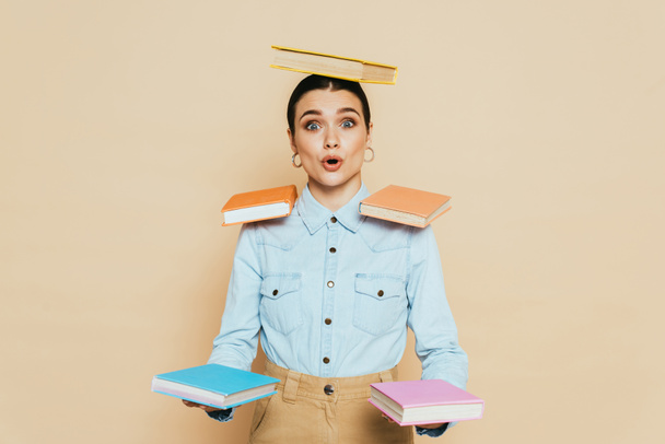 shocked student in denim shirt with books on body isolated on beige - Fotó, kép