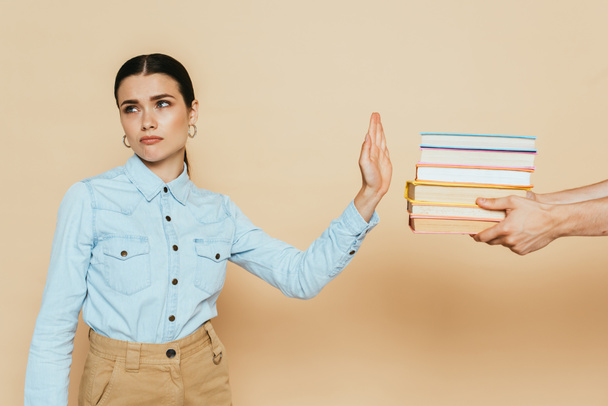 triste studente in camicia di jeans mostrando gesto stop vicino a libri sul beige - Foto, immagini
