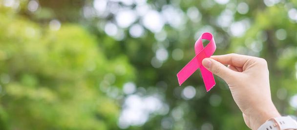 октябрь Месяц награждения за рак молочной железы, взрослая женщина держит за руку розовую ленту на зеленом фоне для поддержки живущих и больных людей. Концепция Международного дня женщин, матерей и борьбы с раком - Фото, изображение