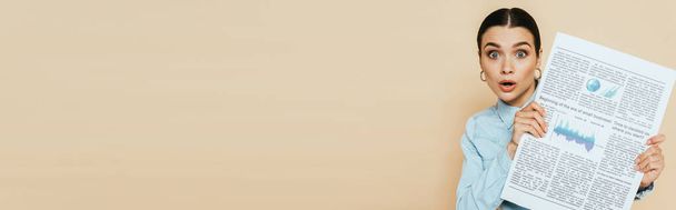 femme brune choquée en chemise denim avec journal d'affaires isolé sur beige, vue panoramique - Photo, image