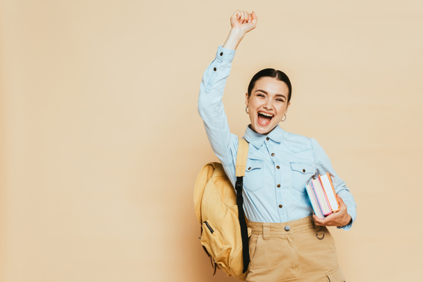 excited brunette student in denim shirt with books and backpack on beige - Foto, Imagen