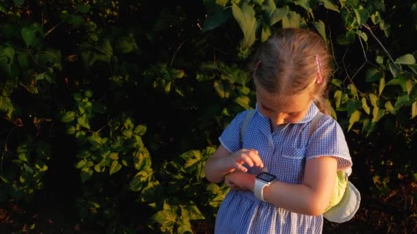 Παιδί που χρησιμοποιεί SmartWatch εξωτερική στο πάρκο. Το παιδί μιλάει στο βίντεο κλιπ στο smartphone. Μαθήτρια που χρησιμοποιεί οθόνη αφής σε ρολόγια περιήγηση στο διαδίκτυο. Έξυπνο ρολόι χειρός με GPS tracker. - Πλάνα, βίντεο