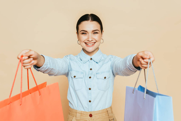 brunetta donna in camicia di jeans dando shopping bags isolato su beige - Foto, immagini