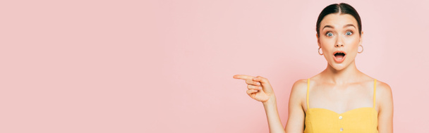 shocked brunette young woman pointing aside on pink, panoramic shot - Fotografie, Obrázek