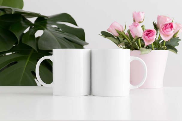 Two mugs mockup with pink roses in a pot and a monstera plant. - Photo, Image