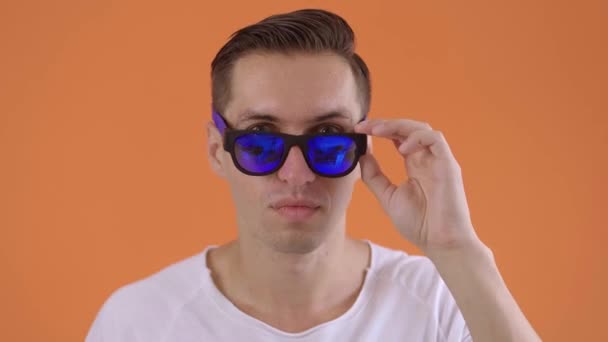 Excited man in surprise shoots sunglasses celebrating success in studio. Portrait of happy person shoots glasses and showing yes gesture. Joyful male holding hands up on orange background. - Felvétel, videó