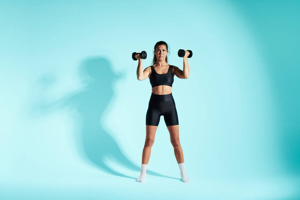 brunette fitness girl on blue background holds dumbbells - Photo, Image