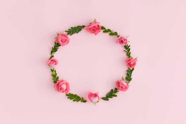 Floral wreath made of pink roses and green branches on a pink background. - Фото, изображение