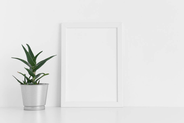 Weiße Rahmen-Attrappe mit einer Aloe Vera im Topf auf einem weißen Tisch. Portraitorientierung. - Foto, Bild