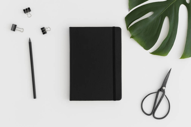 Black notebook mockup with workspace accessories on a white table. - 写真・画像