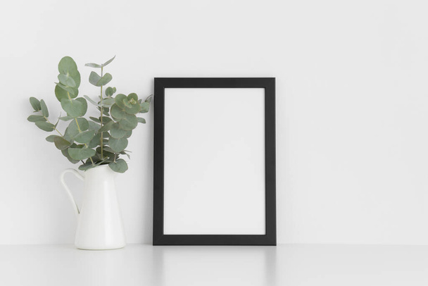 Black frame mockup with a bouquet of eucalyptus in a vase on a white table.Portrait orientation. - Photo, Image