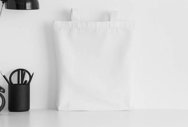 Bolsa de mano blanca maqueta con accesorios de espacio de trabajo en una mesa blanca
. - Foto, imagen