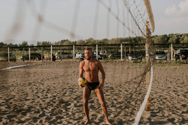 Ein junger kaukasischer Mann in Schwimmunterhosen am Strand mit einem Volleyball in der Hand. Sommer und Meer - Foto, Bild