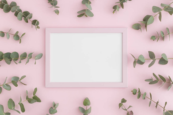 Top view of a pink frame mockup surrounded by branches of eucalyptus on a pink background. - Photo, Image