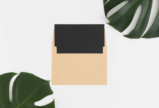 Top view of a black card mockup with monstera leaf decoration on a white table. - 写真・画像
