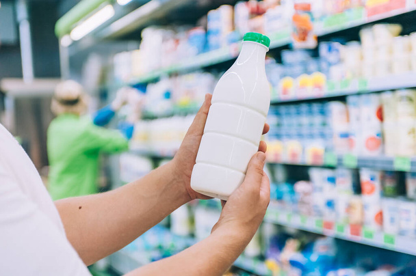 A man holds milk in a plastic bottle in his hands in a supermarket - Fotoğraf, Görsel