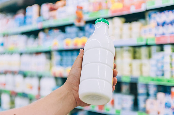 Un hombre sostiene la leche en una botella de plástico en sus manos en un supermercado
 - Foto, Imagen