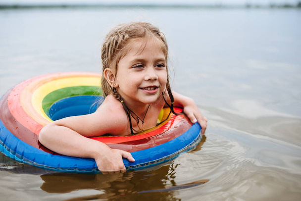 Chica feliz aprende a nadar en un círculo inflable. Vacaciones de verano, calor y agua. El niño nada en un círculo de goma. Vacaciones en la playa con un niño. Seguridad en el agua
 - Foto, Imagen