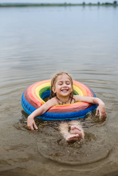 Un enfant heureux nage dans la rivière sur un cercle gonflable coloré. Petite fille mignonne donne naissance tout en nageant dans le lac. Vacances d'été. - Photo, image