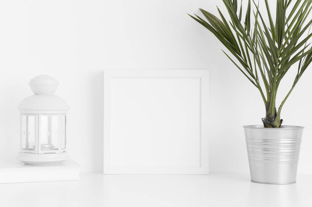 White square frame mockup with a palm in a pot, candle holder and a book on a white table. - Foto, imagen