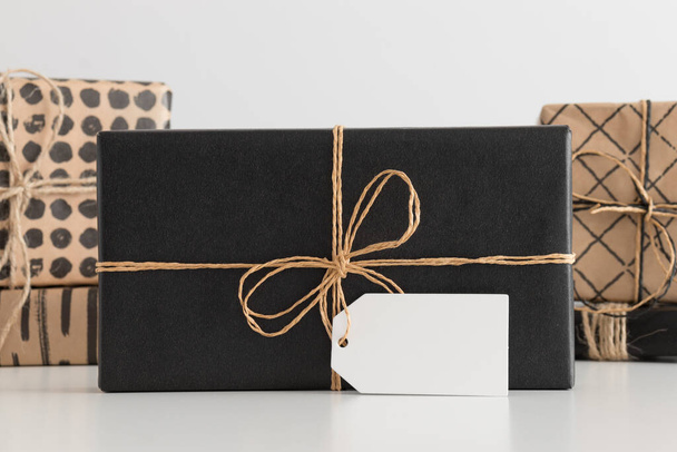 Regalo di Natale nero con tag mockup vuoto con più regali di Natale su una tavola bianca. - Foto, immagini