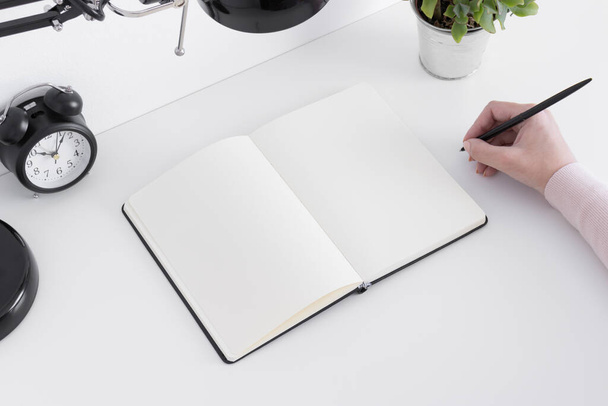 Mockup per notebook aperto con accessori per spazi di lavoro su un tavolo bianco e con donna che prende appunti. - Foto, immagini