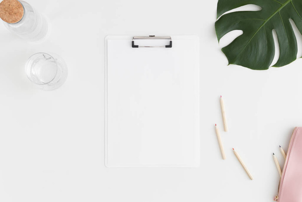 Top view of a white clipboard mockup with  workspace accessories and a monstera leaf on a white table. - Photo, Image