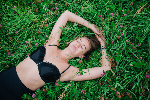 Beautiful girl in black bra and long skirt lies in the grass - Photo, Image