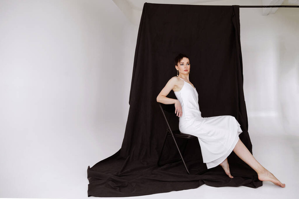 35 éves nő, fehér selyem ruhában, fekete háttérrel a stúdióban - Fotó, kép