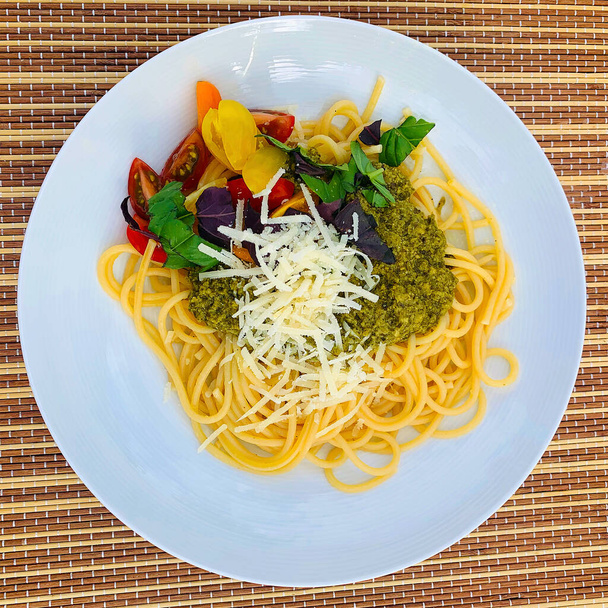 Vollkornspaghetti mit Pesto aus dem Garten, mit frischem, gruenem und rotem Basilikum. Kleinem Tomatenmix und frisch gerieben Pamesan - Foto, imagen