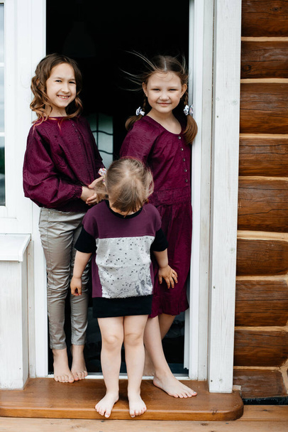 Three little girls went out onto the balcony to breathe fresh air and enjoy the summer nature. Long shiny dark hair. Summer holidays. Carefree childhood. Toning. - Foto, imagen