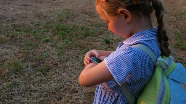 Kind met smartwatch outdoor in het park. Kind aan het praten op vdeo oproep op de smartphone. Schoolmeisje met behulp van touchscreen weergave op horloges surfen op internet. Slim polshorloge met GPS tracker. - Video