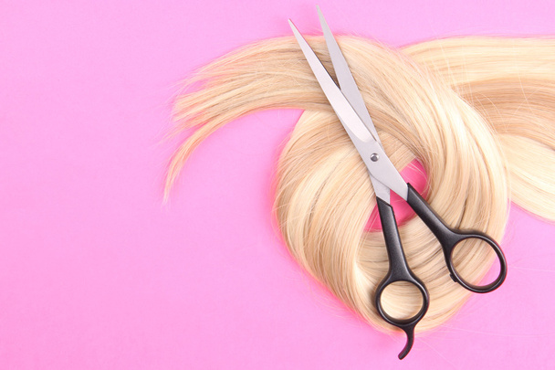 Long blond hair with scissors on pink background - Foto, afbeelding