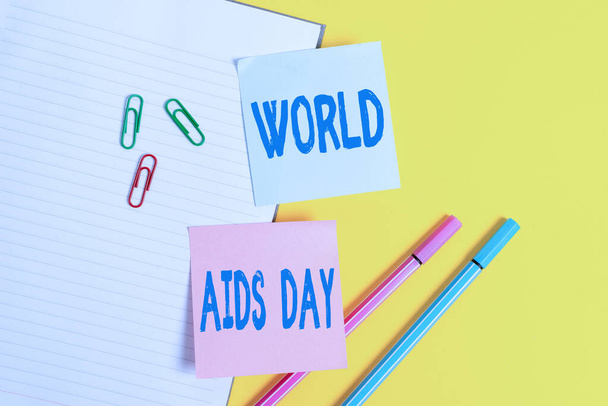 Texto manuscrito Día Mundial del SIDA. Concepto que significa un día internacional para concienciar sobre la pandemia del SIDA Papel azul vacío con clips de papel y lápices en la mesa amarilla
. - Foto, imagen