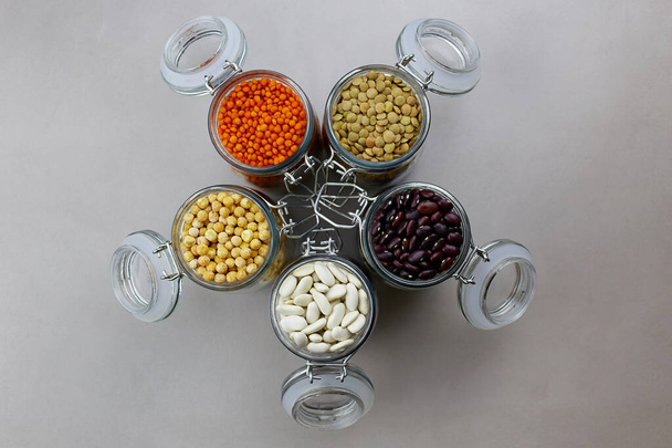 A set of different dried legumes in a glass bowls: red lentils, green lentils, peas, red beans, white beans on grey background - Фото, зображення