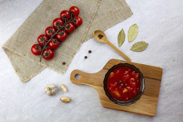 Lecho or canned vegetable salad of red bell peppers and tomatoes in a bowl on a wooden board, gray background - Foto, Bild