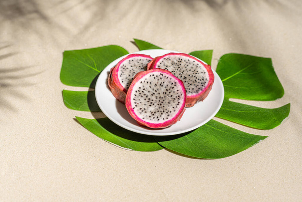 Dragon fruit, pitaya on palm tree leaves on the sand of tropical beach. Exotic food, snack. Summer travel - Fotoğraf, Görsel