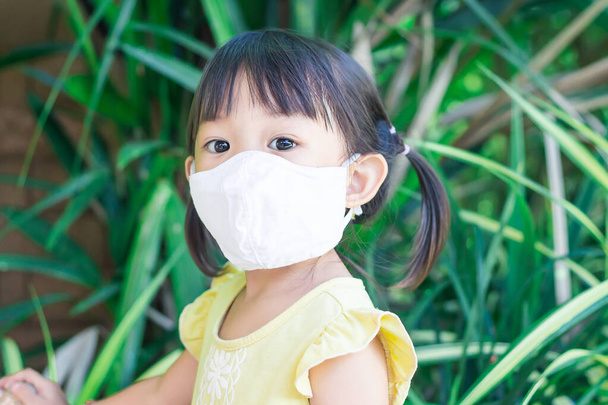 2-3 yaşlarında bir bebeğin portresi. Mutlu Asyalı kız çocuğu gülümsüyor ve kumaş maske takıyor çocuk parkında sürgülü bar oyuncağıyla oynuyor, sosyal mesafe öğreniyor ve çocuk konseptini aktif hale getiriyor.. - Fotoğraf, Görsel