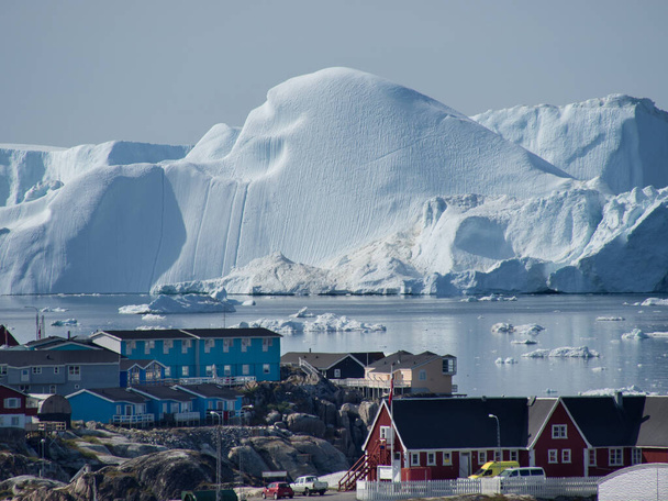 Ogromny lodowiec widać za tradycyjną wioską rybacką na Grenlandii.W zatoce topniejący lód morski widać dryfujący. - Zdjęcie, obraz