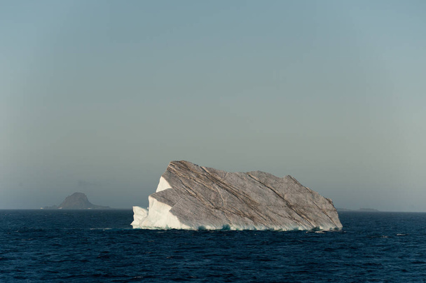 Um grande iceberg deriva no mar no Oceano Ártico, tendo se destacado de uma geleia.Ilhas rochosas podem ser vistas no fundo. - Foto, Imagem