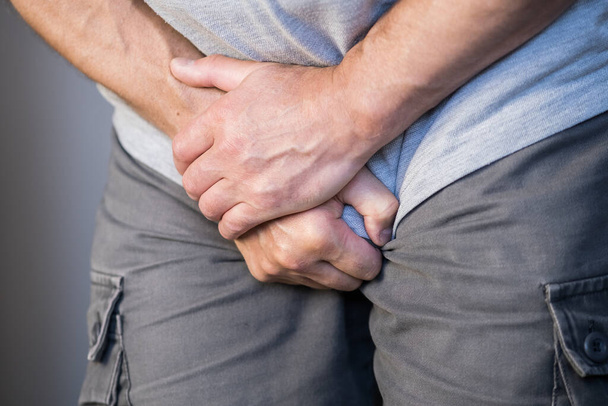 Egy férfi két kézzel tartja az ágyékát, urológiai fájdalom a húgyhólyagban. - Fotó, kép