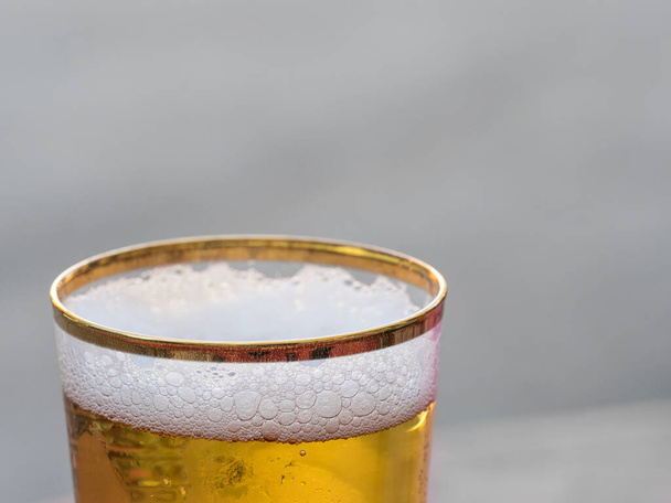 Dicht zicht op het schuim in een nieuw gegoten verguld glas bier. Focus op de voorrand van glas opzettelijk vervagen tot effen achtergrond.Drink - Foto, afbeelding