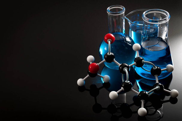 Organic chemistry, science class and STEM research concept with a methyl benzoate molecule on blue chemical solution in chemistry glassware, Erlenmeyer and Boiling (or Florence) flasks with copy space - Photo, Image